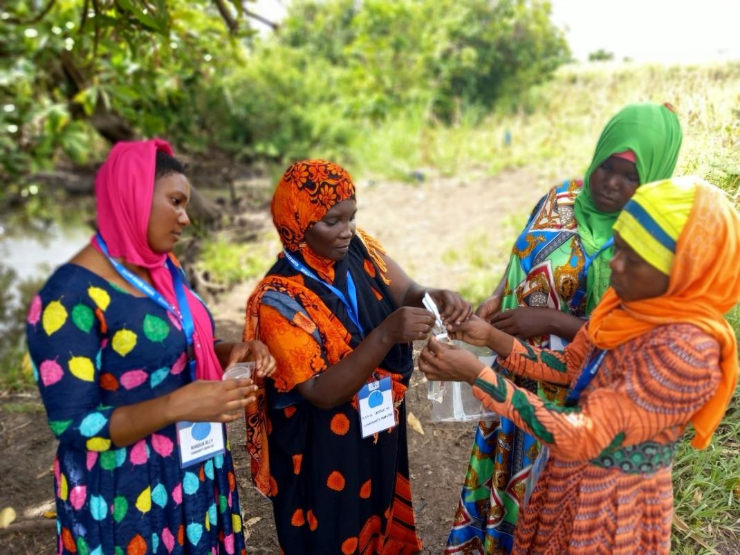 Women Water Watch monitors testing a water sample from a public water source in Tanzania. (c) Women Water Watch