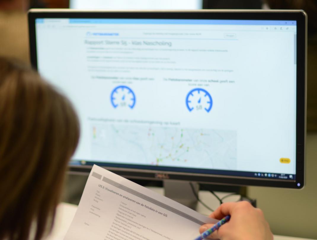 Computerscherm met kaart en data dashboard. Op de voorgrond maakt een persoon aantekeningen op papier.